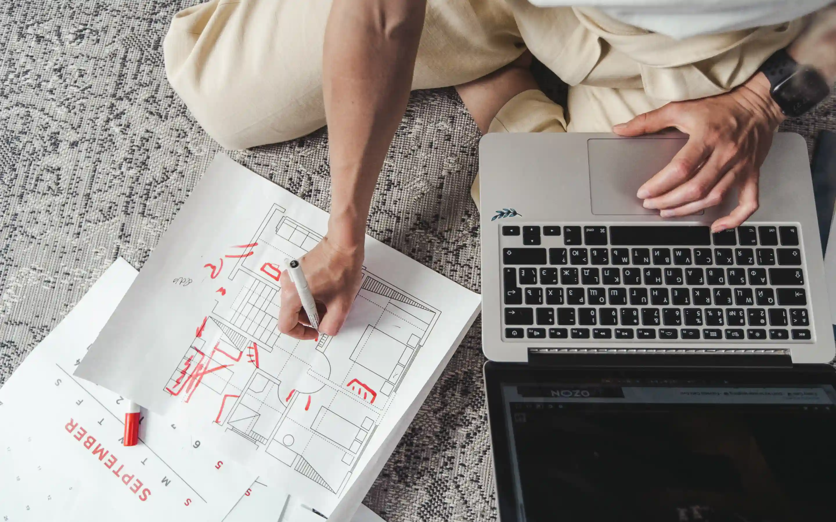 Man planning on laptop and on paper, with a red marker